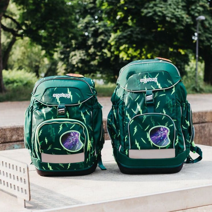 Two backpacks, one one bigger than the other, lying on concrete surface in a park